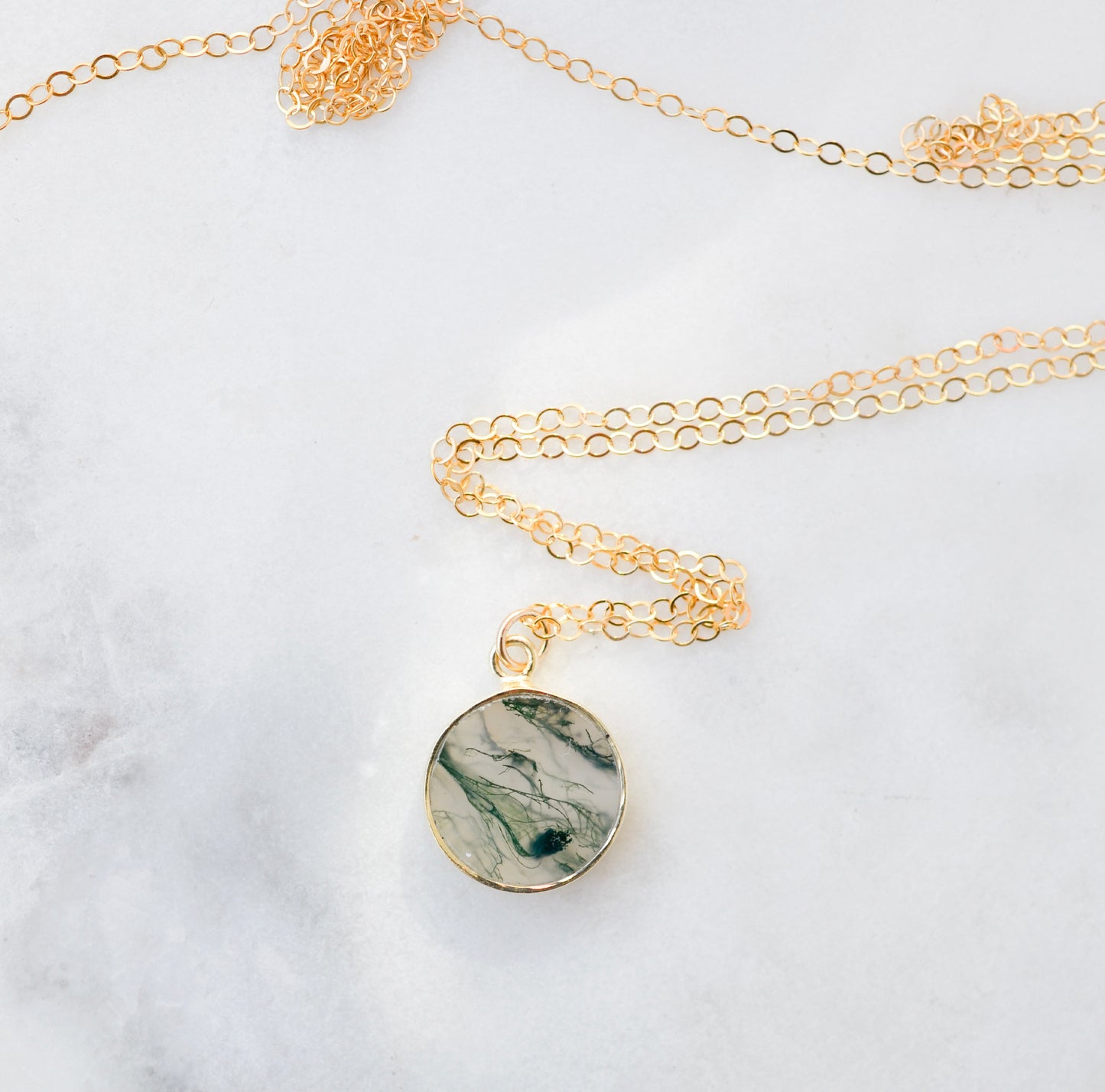 A genuine, natural moss agate circle shaped pendant set on a 14k gold filled chain. This dainty, smooth polished pendant is handmade in Connecticut by Gemnia Jewelry. Makes the perfect give for nature enthusiast, the gardener, or conservationist.