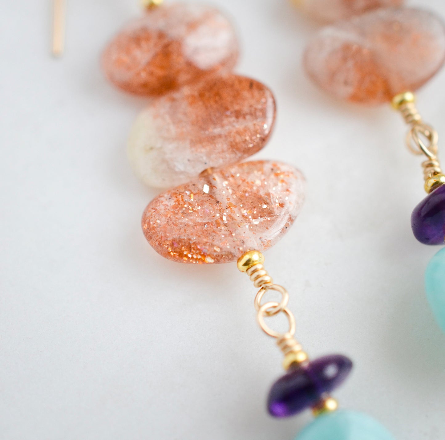 Three sunstone gemstone dangle atop amethyst and amazonite stones. The earring are shown in gold.