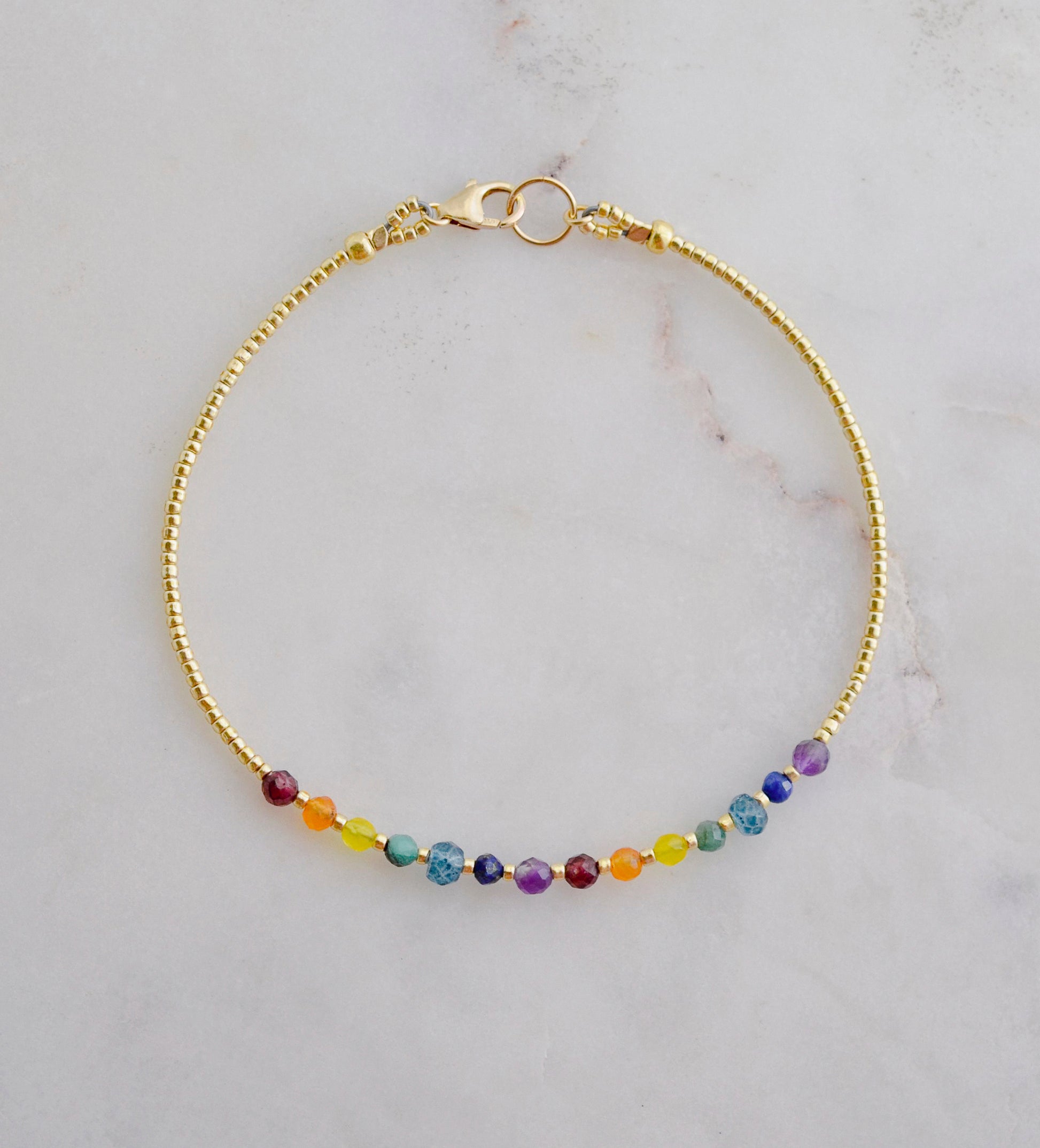 A beaded rainbow bracelet with natural crystal gemstones in the order of the chakras. This gold piece is handmade in Connecticut by Gemnia Jewelry.