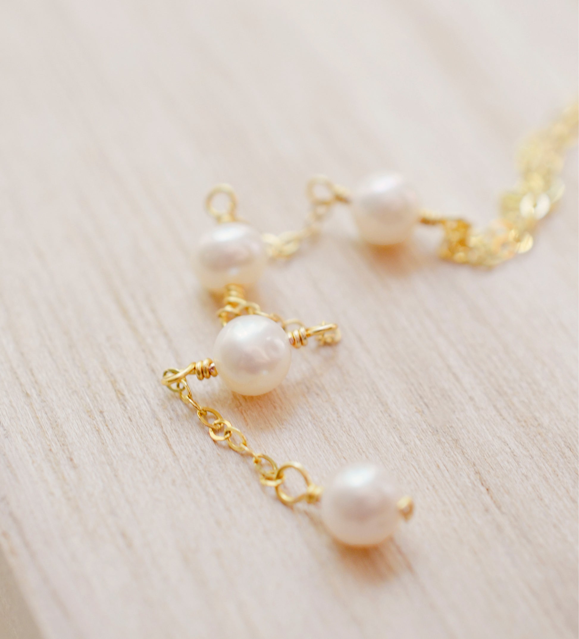 Close up image of the pearls. Four semi-round white freshwater pearls are suspended in a Y-style necklace on a 14k gold filled chain. Each pearl is approximately one inch apart. This necklace is also available in sterling silver.