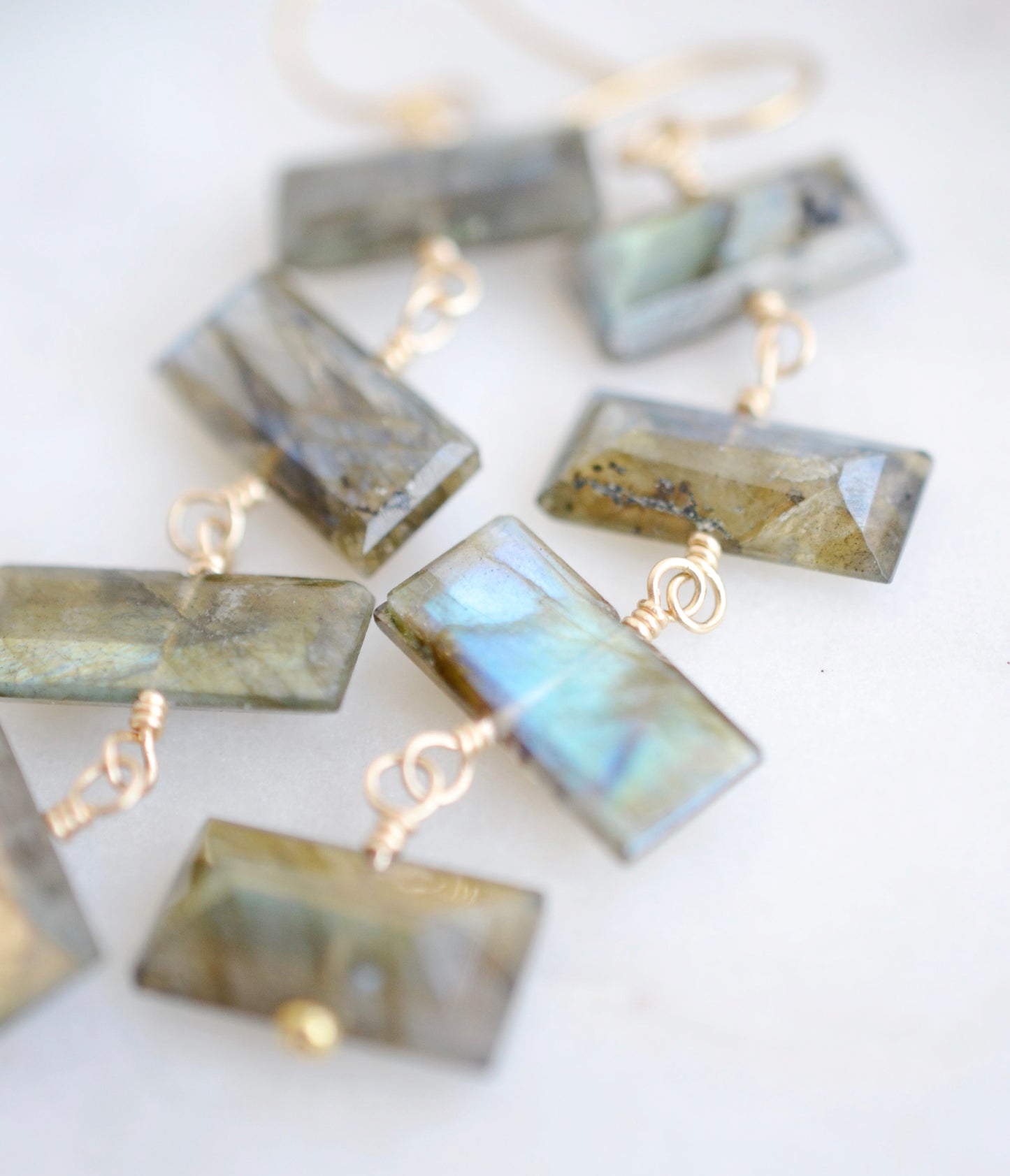 Close up image: Four faceted emerald cut labradorite gemstones dangle in these 14k gold filled earrings. Each stone flashes blue or green.