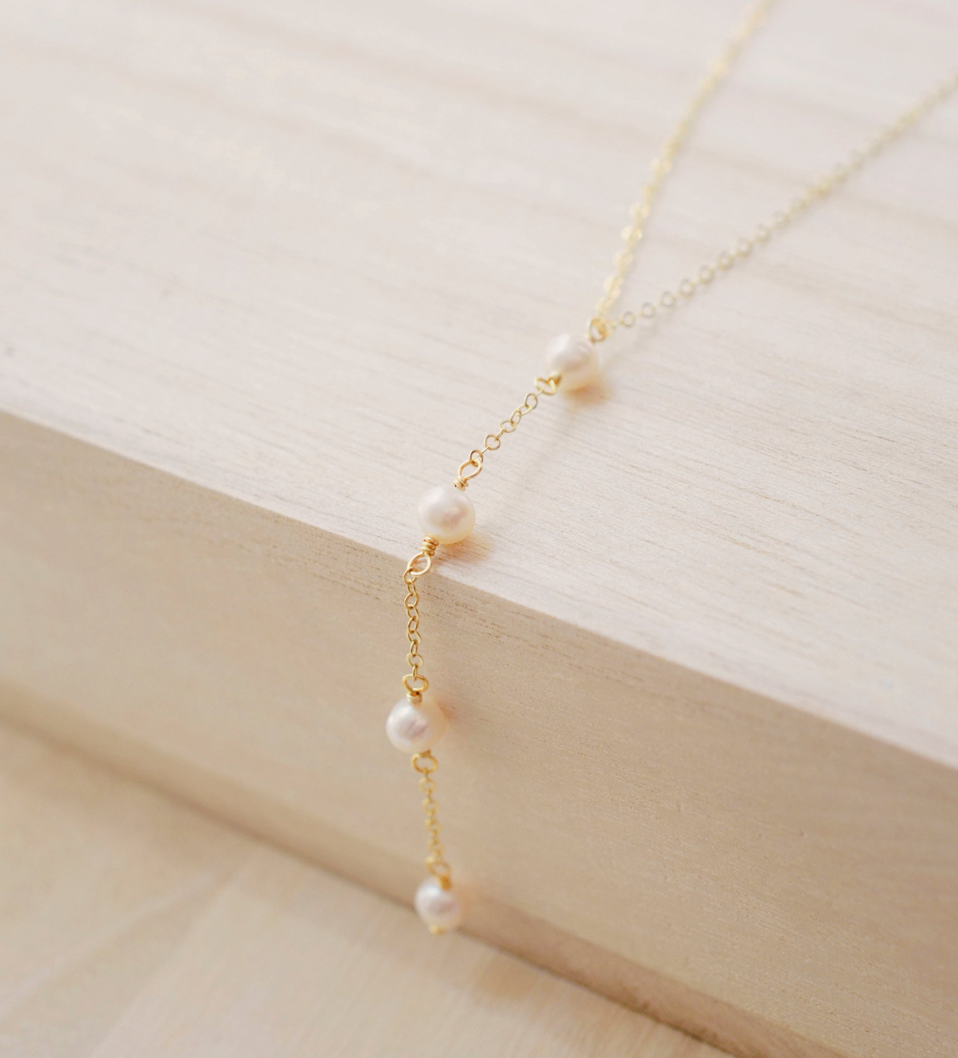 Four semi-round white freshwater pearls are suspended in a Y-style necklace on a 14k gold filled chain. Each pearl is approximately one inch apart. This necklace is also available in sterling silver.