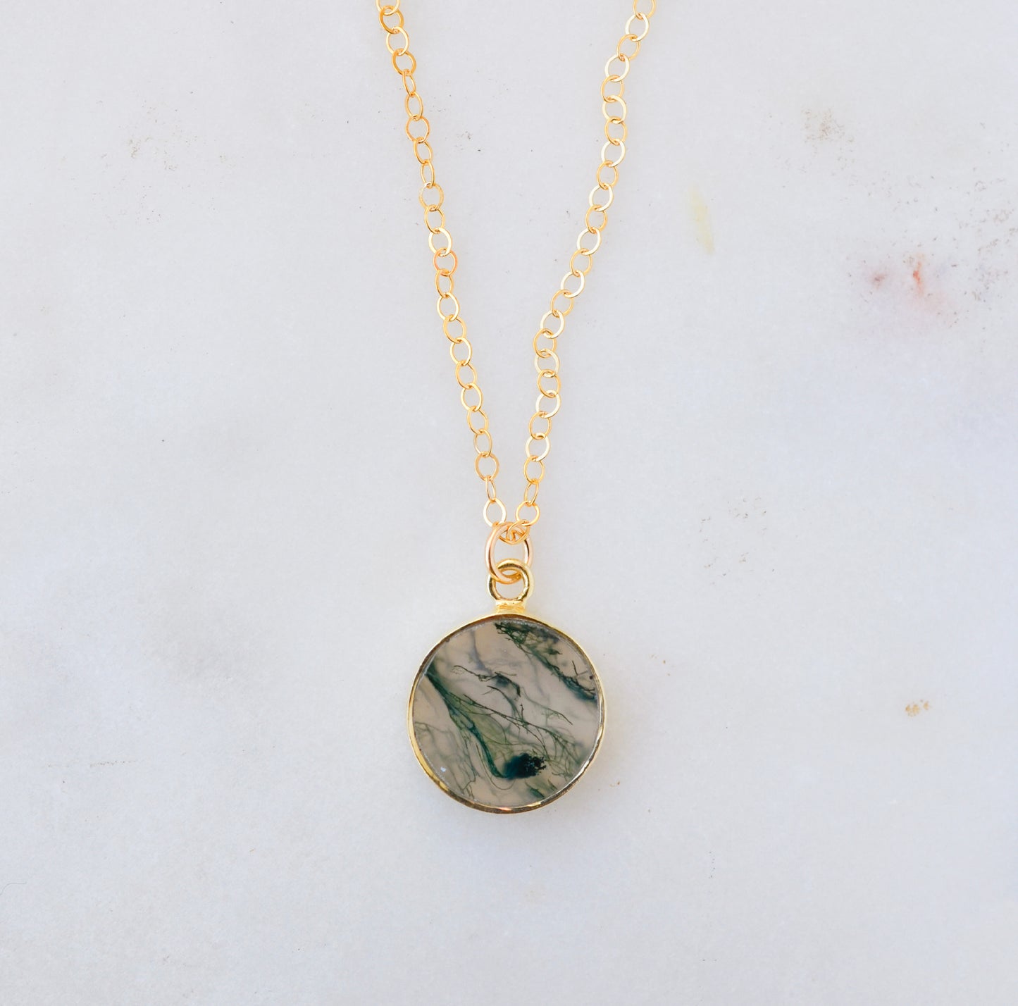 A genuine, natural moss agate circle necklace set on a 14k gold filled chain. This boho, dainty, smooth polished pendant is handmade in Connecticut by Gemnia Jewelry.