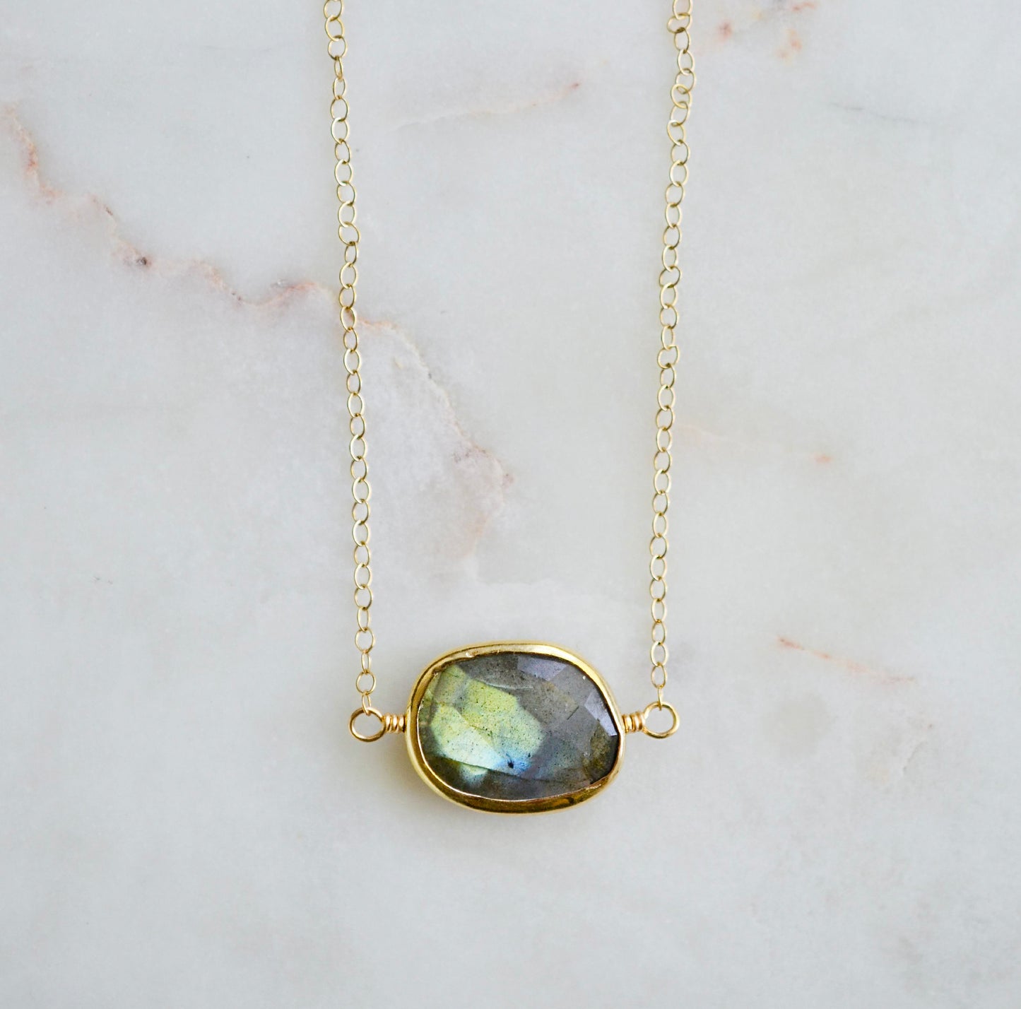 A faceted, natural labradorite pendant bezeled in gold and set on a 14k gold filled chain. This necklace is also available in sterling silver. The stone is oval in shape and flashes blue, green, or yellow.