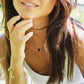 Woman wearing a necklace with a blue lapis lazuli pendant and gold star and heart layered bracelets.