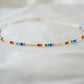 Tiny stones arranged in the order of the seven chakras or rainbow colors. Colors include: purple, blue, aqua, green, yellow, orange, and red. Close up of the gold style.
