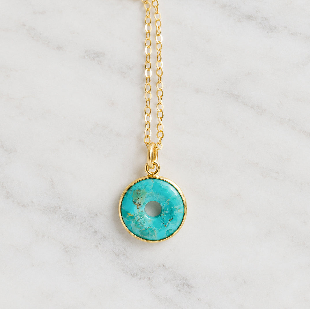 A closeup image of a circular donut pendant in turquoise. The stone is smooth polished and suspended from a dainty, minimalist 14k gold filled cable chain. Also available in sterling silver. Handmade by Gemnia in New England.