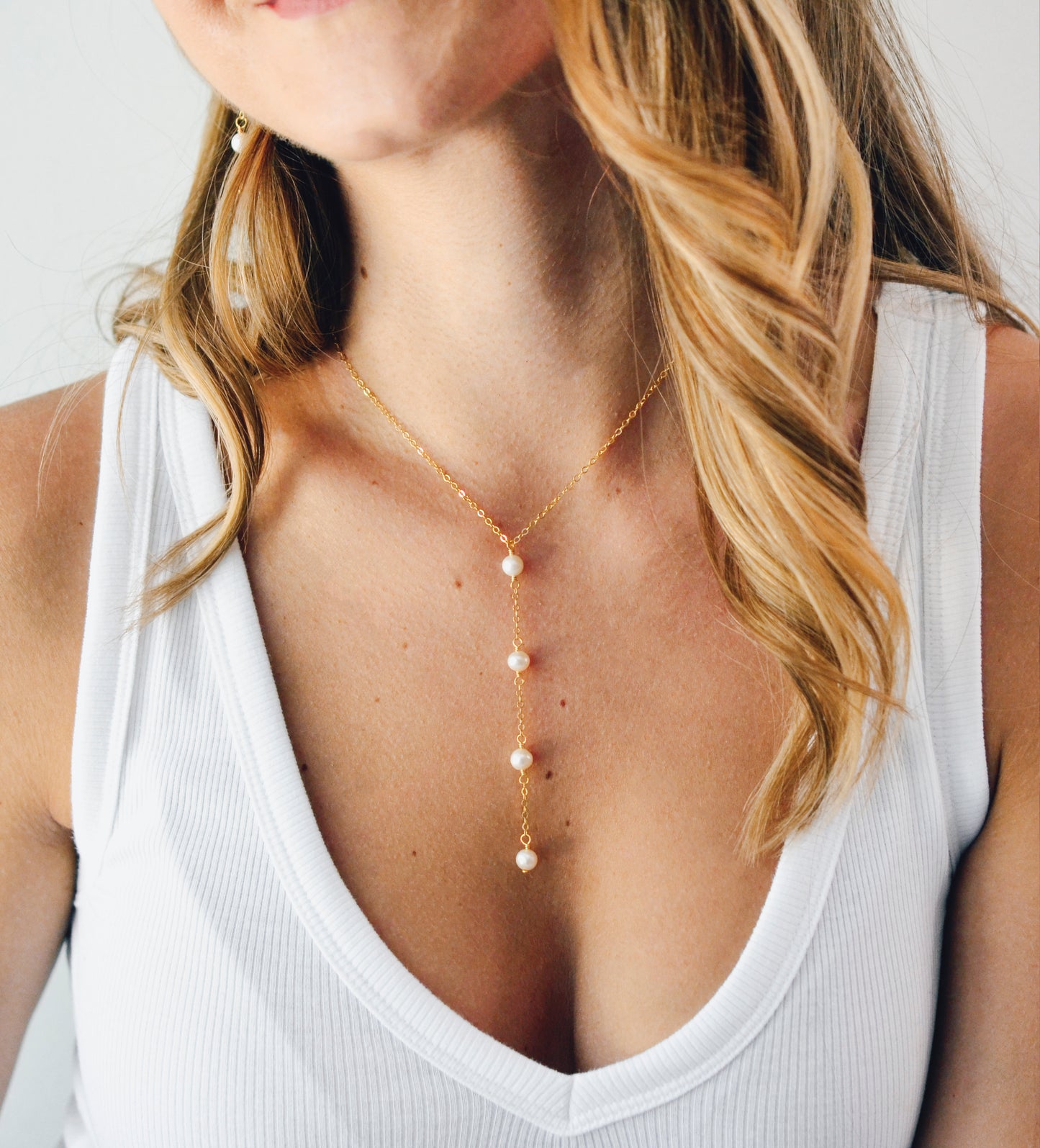 Modeled image. Four semi-round white freshwater pearls are suspended in a Y-style necklace on a 14k gold filled chain. Each pearl is approximately one inch apart.
