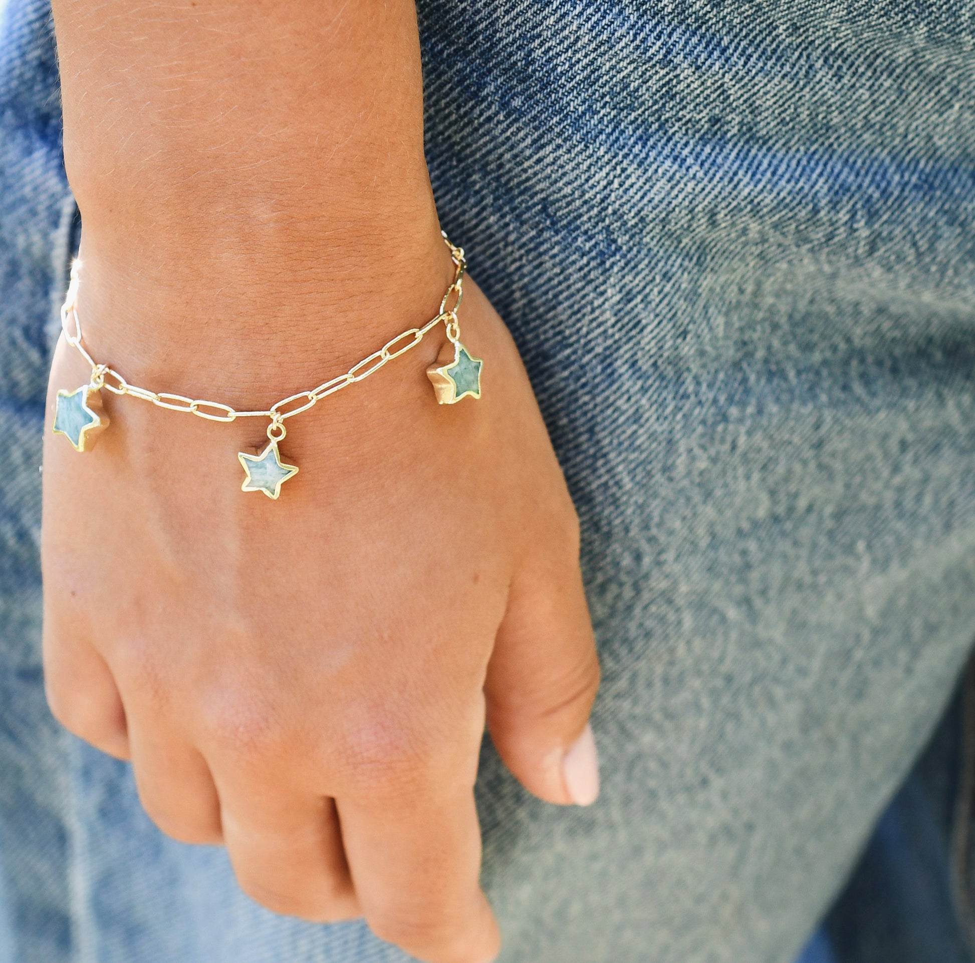 Gold bracelet with Amazonite gemstone star charms on a wrist against a denim background.