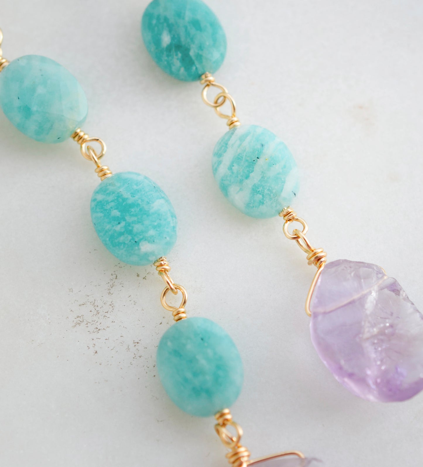 Three Amazonite faceted oval stones hang over raw, pale purple Amethyst crystals. Shown in the 14k gold filled style. Close up.