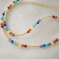 Tiny stones arranged in the order of the seven chakras or rainbow colors. Colors include: purple, blue, aqua, green, yellow, orange, and red. Close up of the gold style.