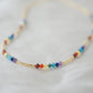 Tiny stones arranged in the order of the seven chakras or rainbow colors. Colors include: purple, blue, aqua, green, yellow, orange, and red. Close up of the gold style.