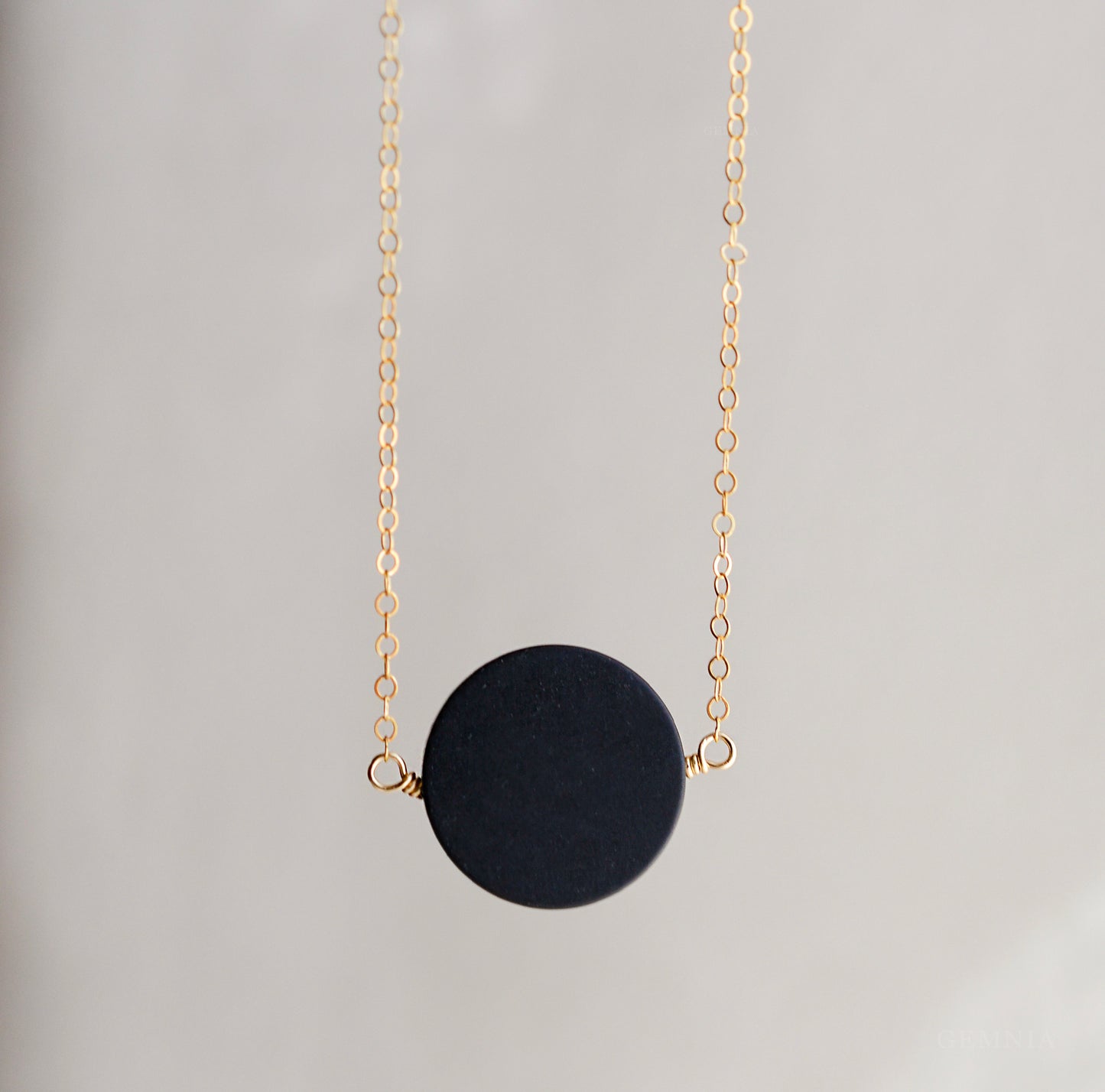 A smooth polished large black onyx coin stone set on a 14k gold filled chain. This necklace is handmade by Gemnia Jewelry in Connecticut.