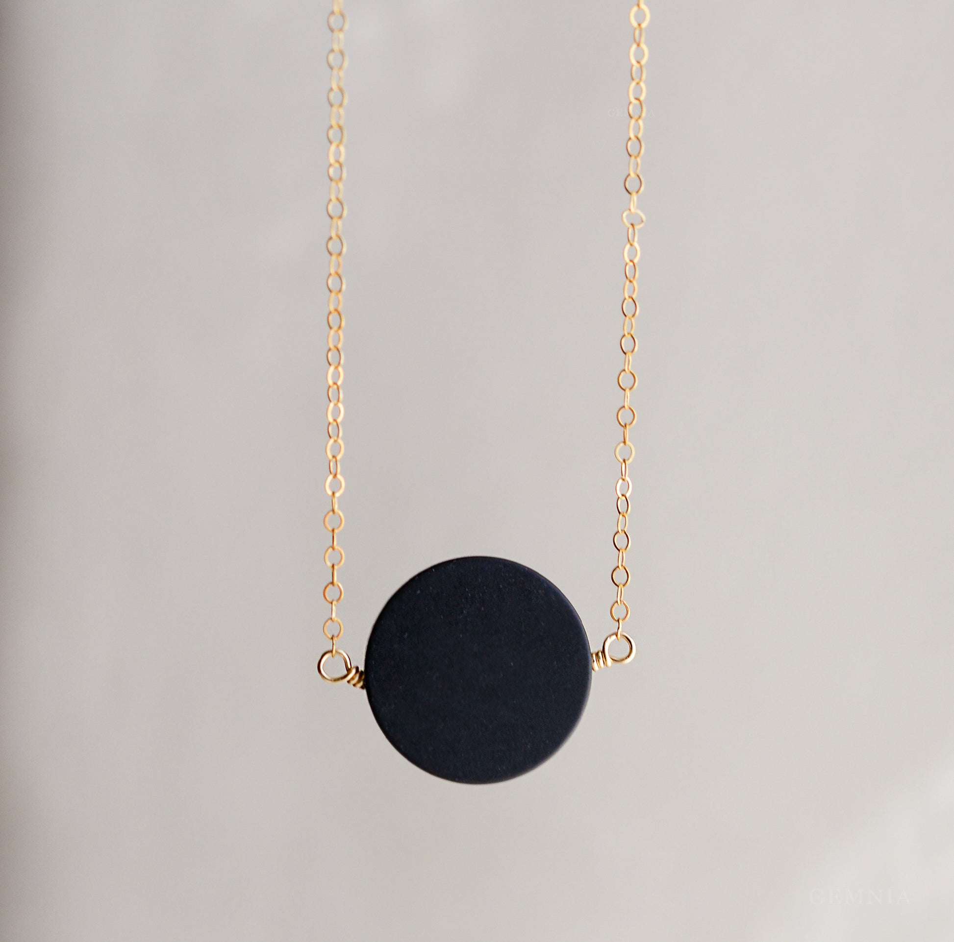 A smooth polished large black onyx coin stone set on a 14k gold filled chain. This necklace is handmade by Gemnia Jewelry in Connecticut.