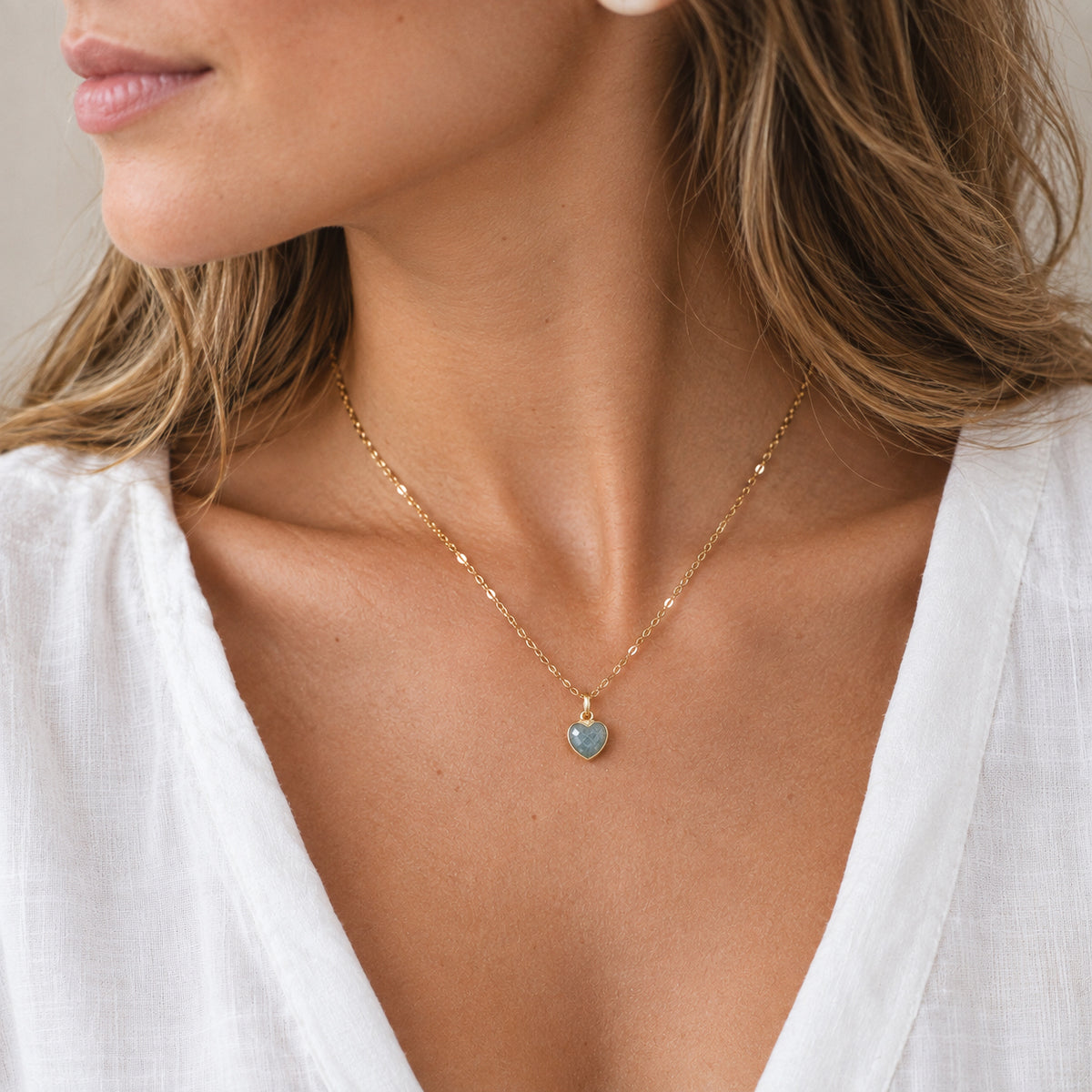 A woman wearing a dainty handmade natural blue aquamarine everyday heart pendant on a 14k gold filled chain necklace. This jewelry is handmade by Gemnia in Connecticut, USA.