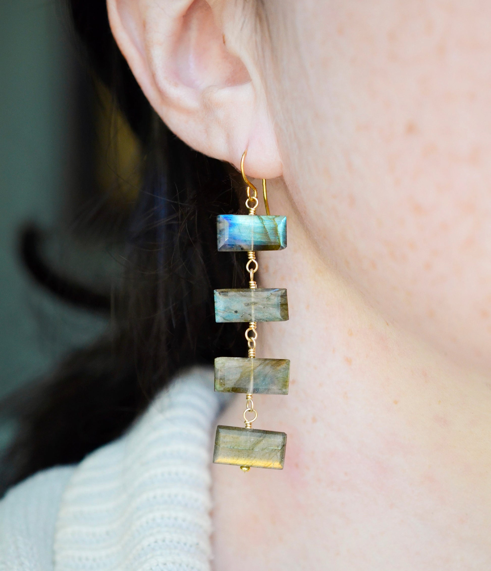 A person wearing long labradorite dangle earrings with gold and silver colors.