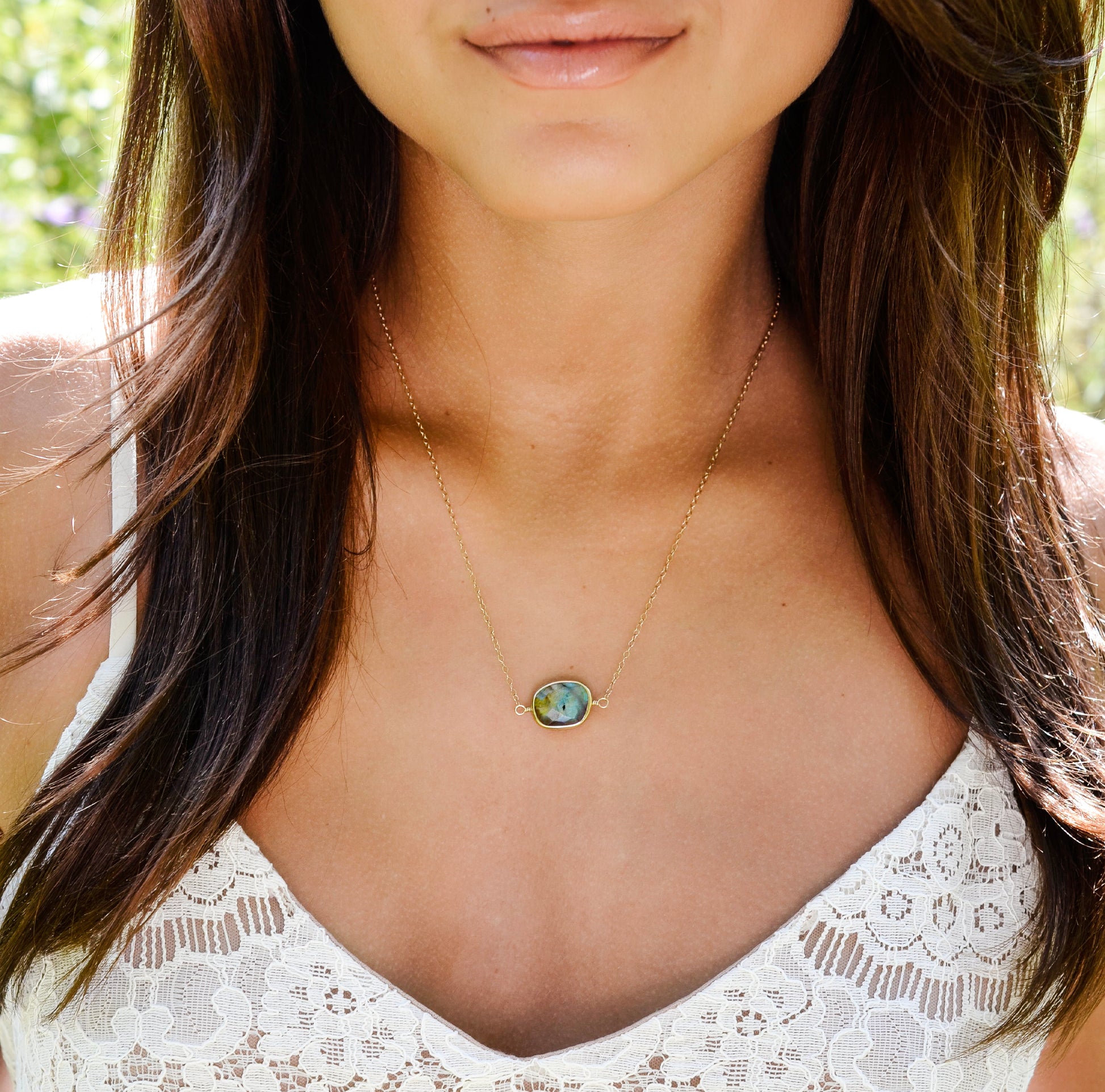 A modeled image of a woman wearing a gold Labradorite necklace. The handmade pendant pendant is bezeled in gold and set on a 14k gold filled chain. This necklace is also available in sterling silver. The stone is oval in shape and flashes blue, green, or yellow.