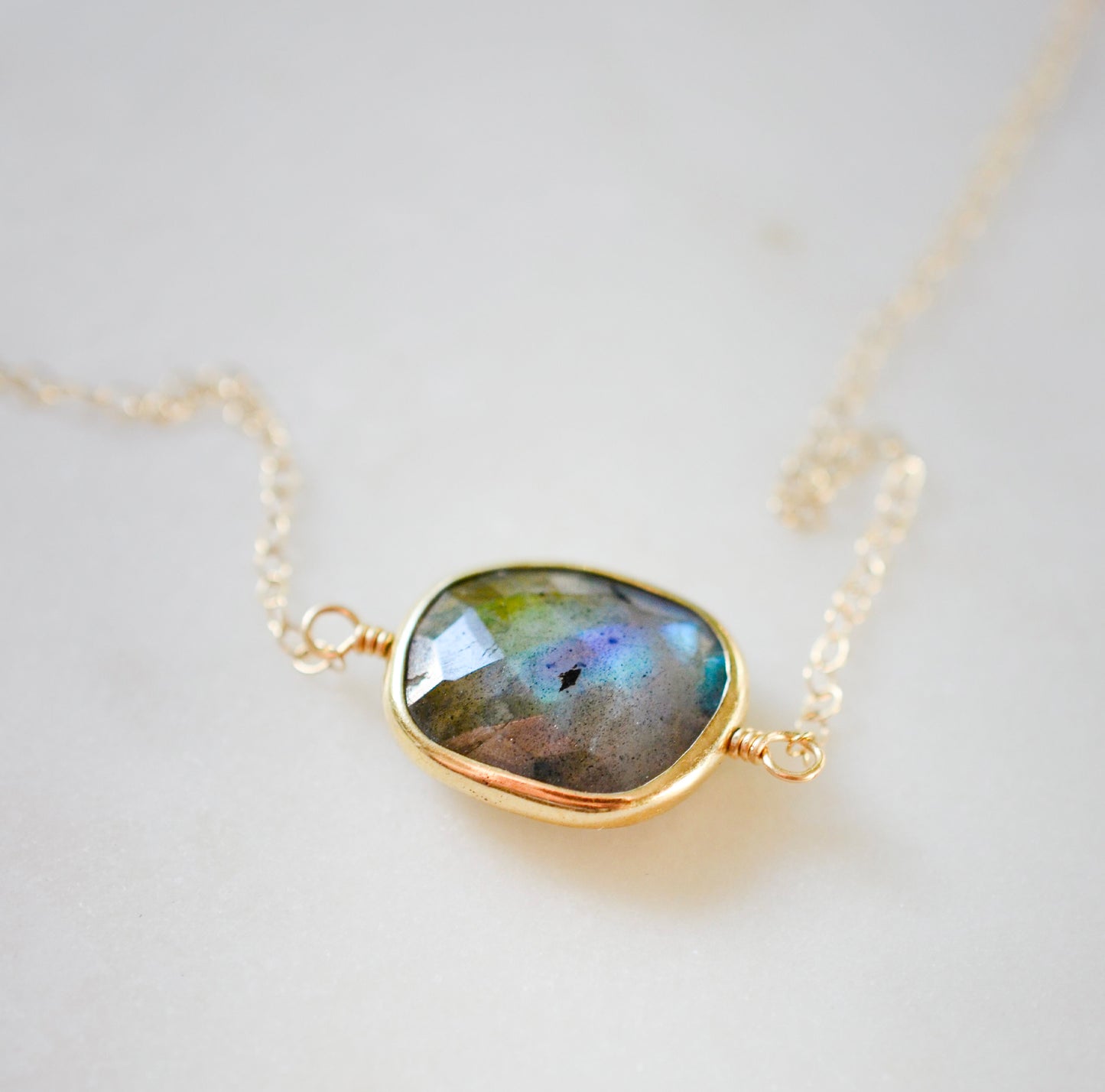 A gold Labradorite necklace. The handmade pendant pendant is bezeled in gold and set on a 14k gold filled chain. This necklace is also available in sterling silver. The stone is oval in shape and flashes blue, green, or yellow.