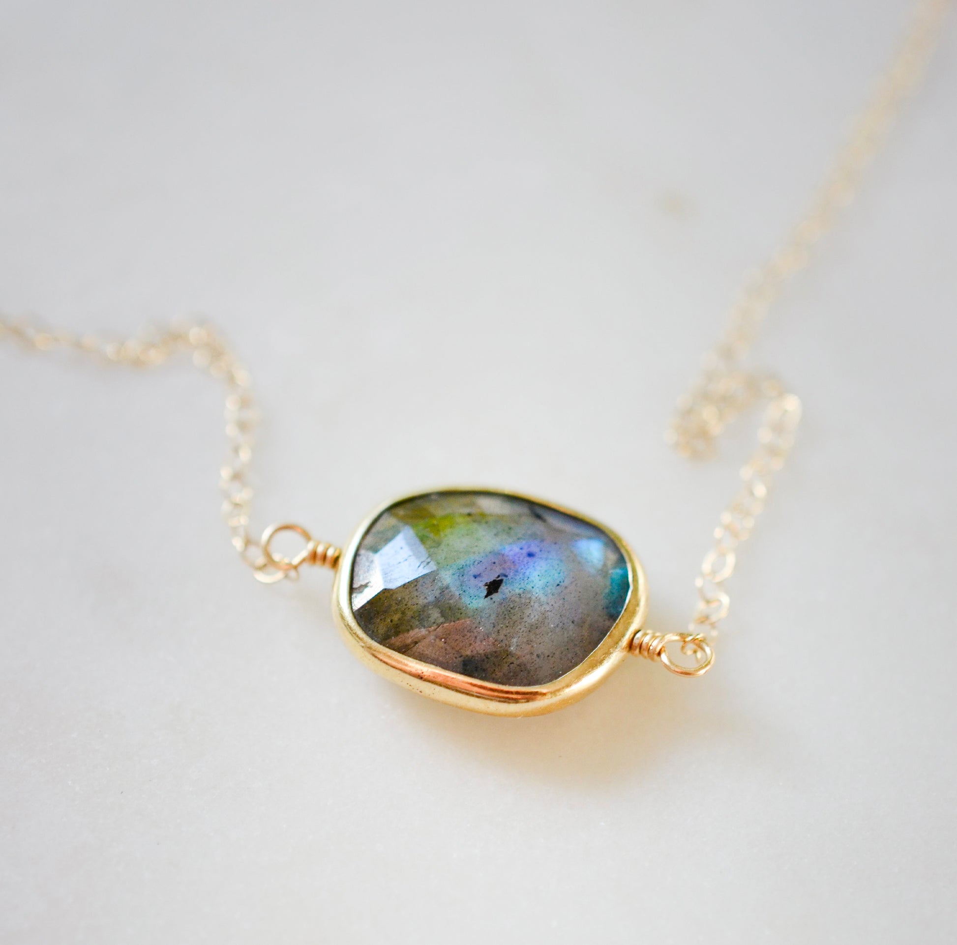 A gold Labradorite necklace. The handmade pendant pendant is bezeled in gold and set on a 14k gold filled chain. This necklace is also available in sterling silver. The stone is oval in shape and flashes blue, green, or yellow.