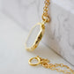 Side view of bezel. A smooth polished natural, white mother of pearl slice has been set in a 24k gold electroplated bezel and suspended from a 14k gold filled chain. The shell shimmers in shades of white, silver, and pink.
