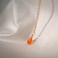 Natural orange triangular shaped Carnelian gemstone set onto a gold chain. Side view.