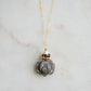 A handmade gemstone pendant featuring a carved obsidian lotus. Garnet, pearl, and gold beads decorate its top. The chain is 14k gold filled.