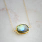 Necklace with a gold-framed Labradorite stone on a light background. The handmade pendant is bezeled in gold and set on a 14k gold filled chain. This necklace is also available in sterling silver. The stone is oval in shape and flashes blue, green, or yellow.