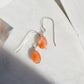 A pair of sterling silver sunstone earrings with a teardrop shape and a reflective orange appearance, displayed against a light background.