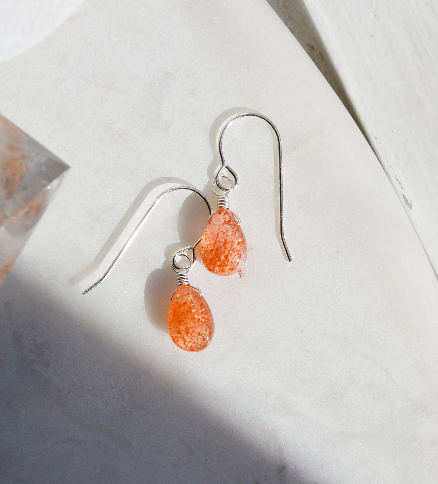 A pair of sterling silver sunstone earrings with a teardrop shape and a reflective orange appearance, displayed against a light background.