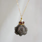 A handmade gemstone pendant featuring a carved obsidian lotus. Garnet, pearl, and gold beads decorate its top. The chain is 14k gold filled.