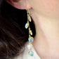 Modeled image. These handmade earrings feature blue and white natural stone hearts bezeled in gold. Each gemstone is a different color and includes: labradorite, larimar, mother of pearl, aquamarine, and rainbow moonstone. Long and light weight they make the perfect romantic gift. They are 3 inches long.