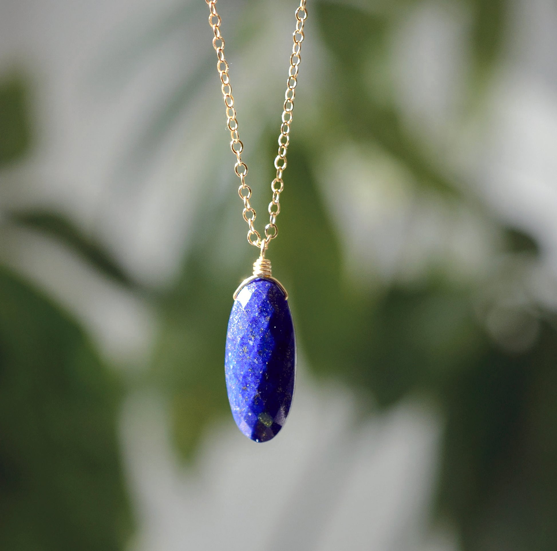 A genuine natural blue Lapis Lazuli faceted oval stone pendant hangs from a 14k gold filled chain. This necklace is handmade in Connecticut by Gemnia Jewelry.