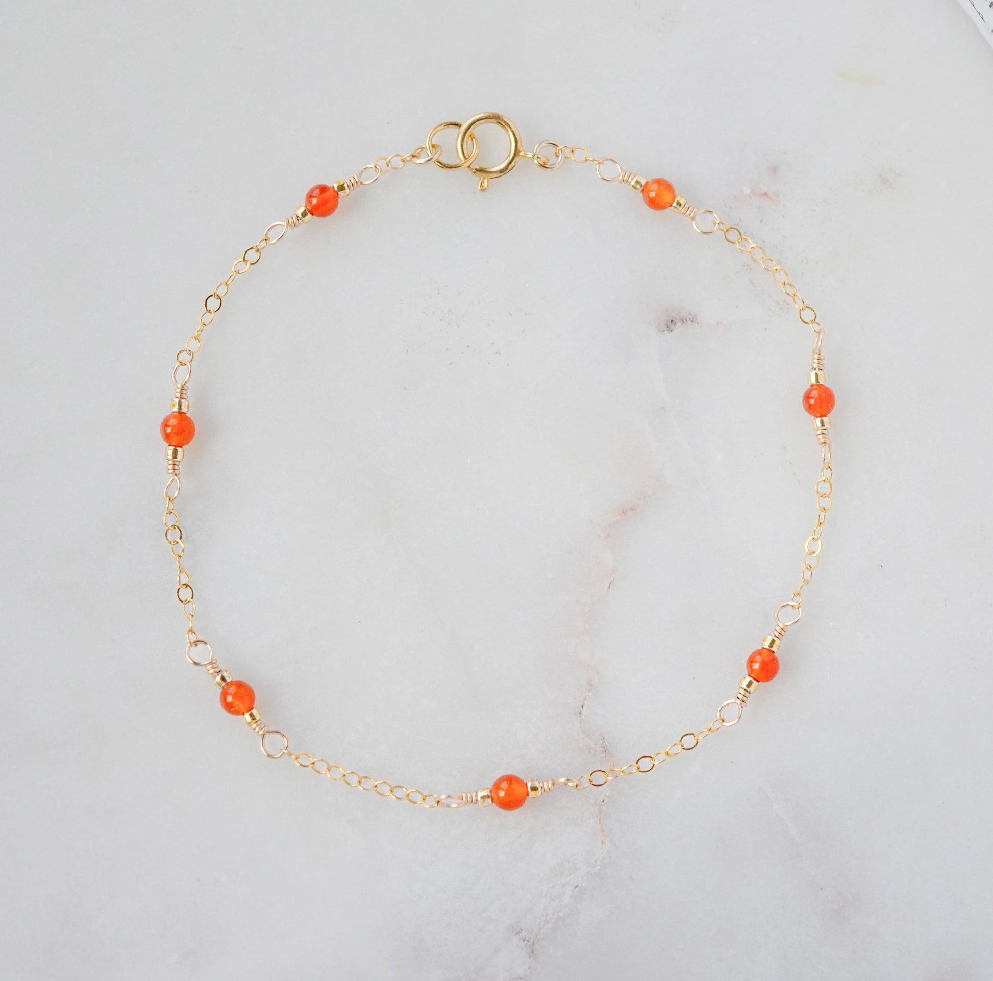 A gold-colored bracelet featuring orange carnelian stones on a 14k gold filled chain.