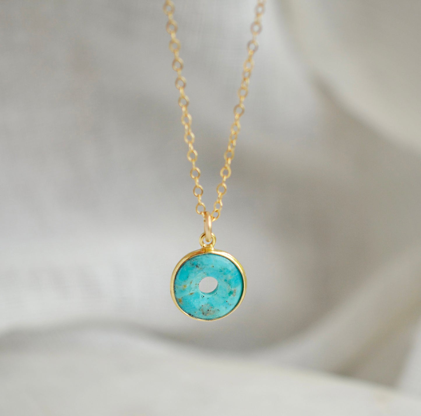 This necklace is handmade with a turquoise stone cut in a doughnut shape then suspended from a 14k gold filled chain. Also available in sterling silver. 