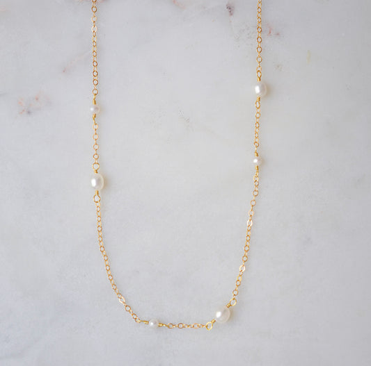 Gold necklace with small dainty pearls on a marble surface.
