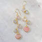 Long pink stone heart earrings in 14k gold filled. There are five heart crystal dangles hanging from a simple chain forming a cluster. The stones include: rose quartz, mother of pearl, pink opal, and rainbow moonstone. They are approximately three inches long.