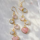 Long pink stone heart earrings in 14k gold filled. There are five heart crystal dangles hanging from a simple chain forming a cluster. The stones include: rose quartz, mother of pearl, pink opal, and rainbow moonstone. They are approximately three inches long.