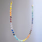 Rainbow chakra gemstone necklace. Crystals are beaded together in this pattern: yellow, orange, red, purple, blue, aqua, green. The gold style is shown. Close up.