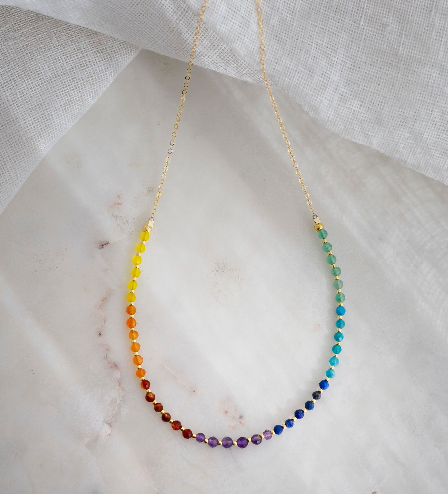 The single rainbow style beaded necklace is shown in gold.