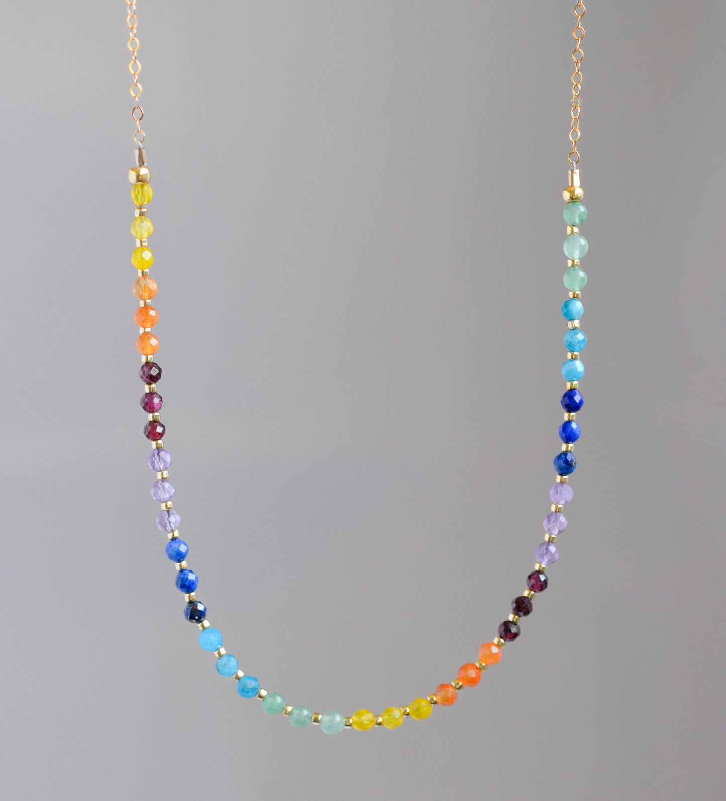 Rainbow chakra gemstone necklace. Crystals are beaded together in this pattern: yellow, orange, red, purple, blue, aqua, green. The gold style is shown.