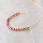 Natural pink Rhodochrosite beaded handmade necklace shown in 14k gold filled. The gemstones vary in shades of pink, peach, white, and gray and are faceted rondelle shape. They span approximately 4 inches across the front of the necklace, then attach to a dainty cable chain. Also available in sterling silver.