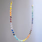 Rainbow chakra gemstone necklace. Crystals are beaded together in this pattern: yellow, orange, red, purple, blue, aqua, green. The gold style is shown. Close up.
