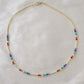 Tiny stones arranged in the order of the seven chakras or rainbow colors. Colors include: purple, blue, aqua, green, yellow, orange, and red. Close up of the gold style.