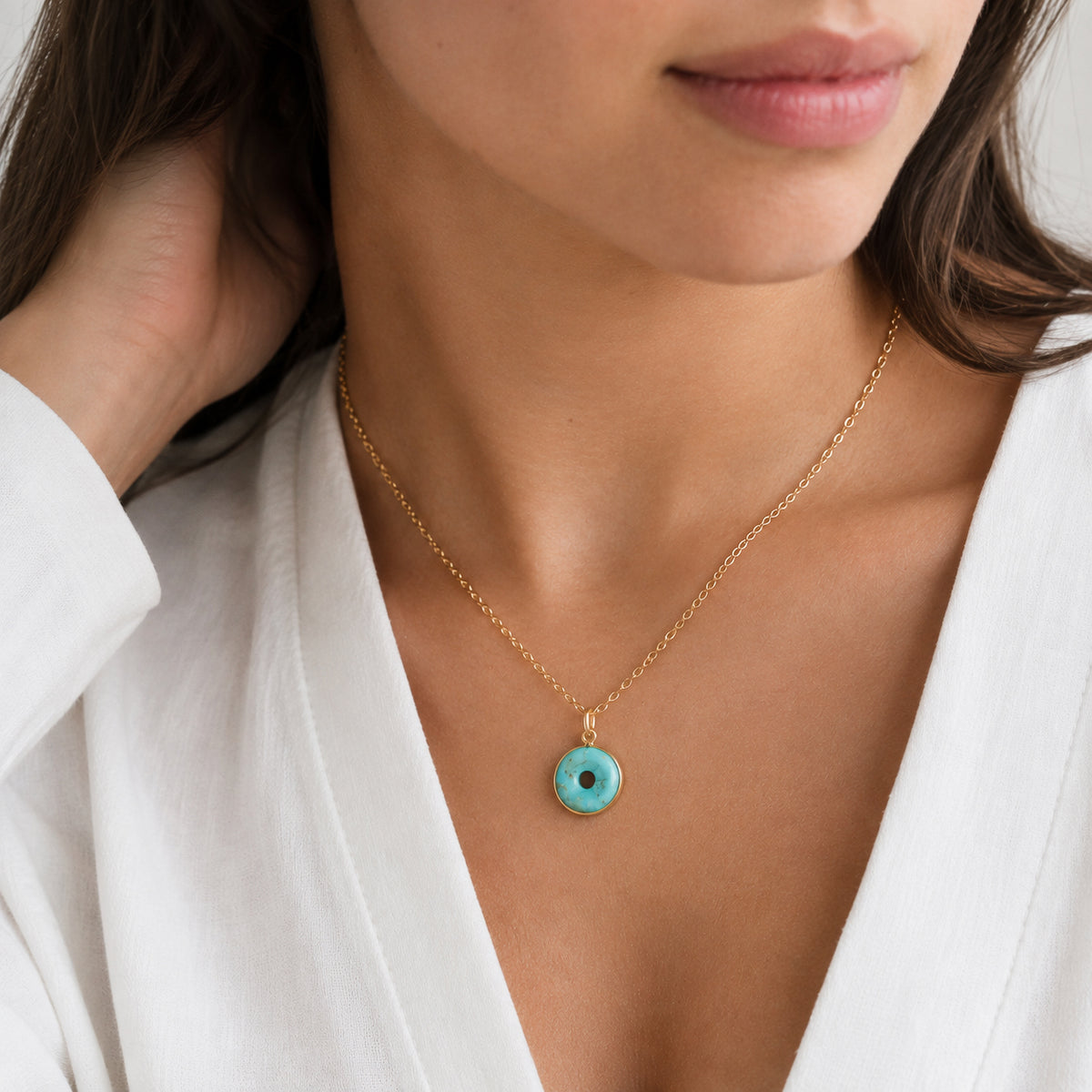 A woman wearing a blue turquoise pendant that is a donut shape (circle with a hole in the center). The stone is suspended from a delicate 14k gold filled chain. This necklace is handcrafted by Gemnia and also available in sterling silver.