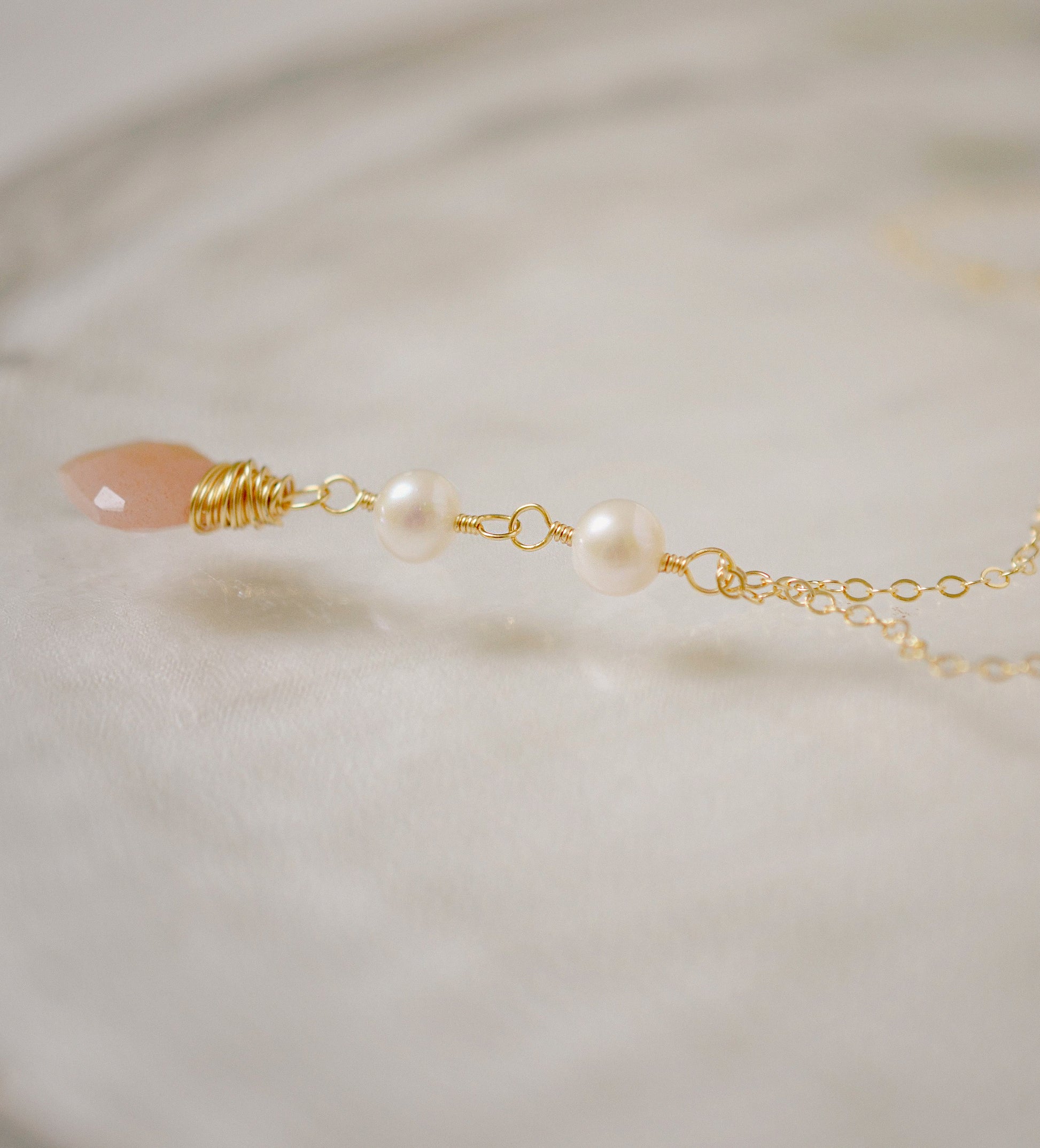 Side View. Two white semi-round pearls hang over a natural peach Moonstone faceted drop. The gold style pendant is shown.