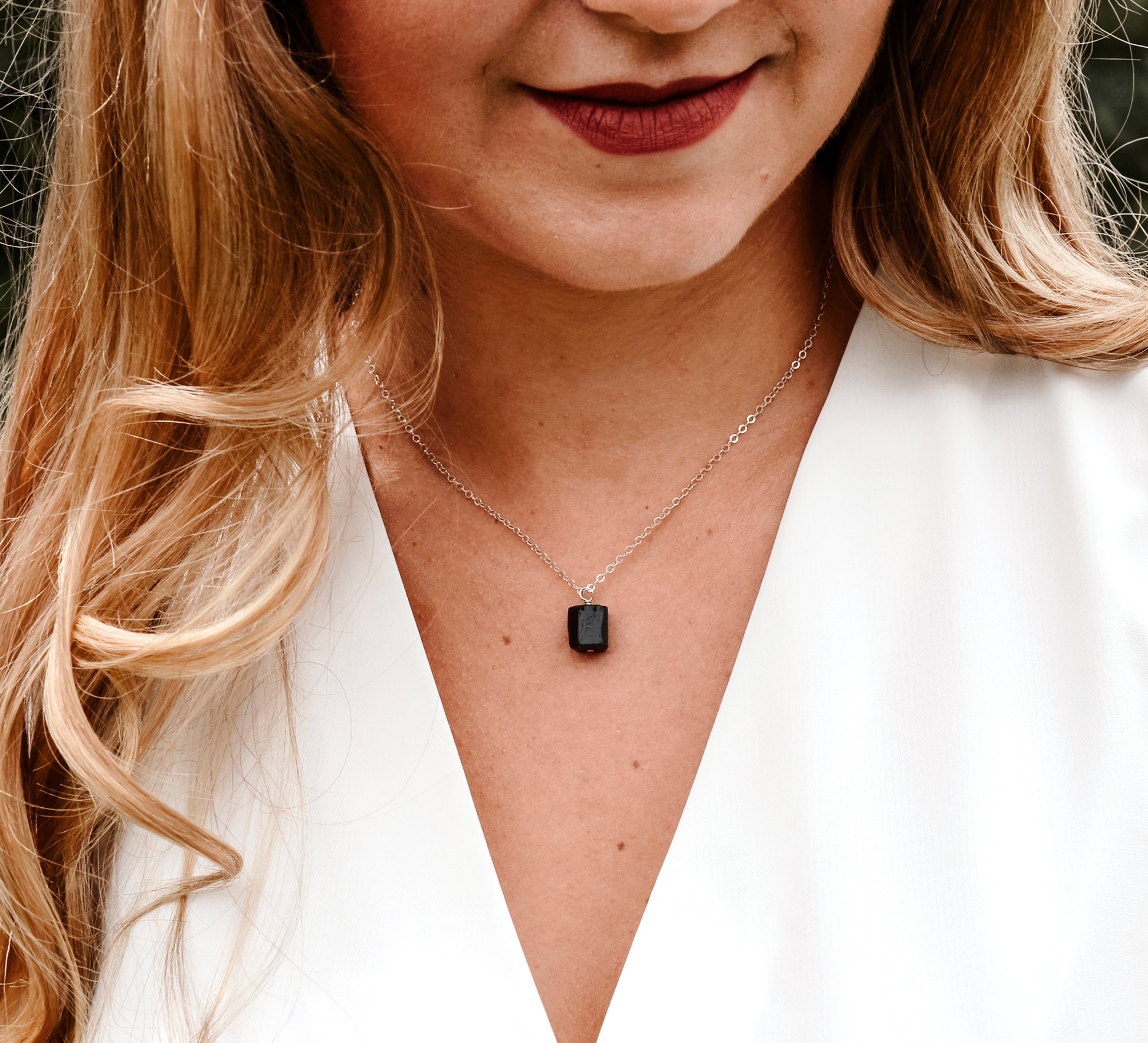 A modeled image of a woman wearing a rough, genuine, black tourmaline crystal necklace in sterling silver. The minimalist jewelry is handmade in Connecticut. 