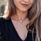 A woman is wearing a natural white howlite necklace. The stone is round with natural gray marbling and set on a 14k gold filled chain. Also available in sterling silver. 