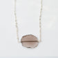 An irregular oval shape, smooth polished Smokey Quartz stone set onto a 14k gold filled chain. The stones edges are raw and irregular. The stone is mostly clear and may show natural inclusions.